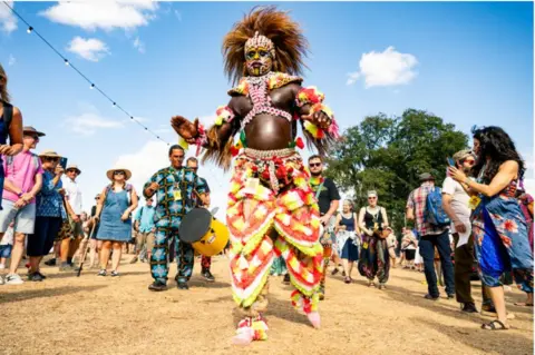 Garryjonesphotography A man in a colourful outfit dances as a man plays a drum behind him