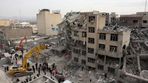 Reuters Iranian rescue workers work among the rubble of damaged residential buildings in central Tehran, Iran, 12 March 2026. A joint Israeli and US military operation continues to target multiple locations across Iran since the early hours of 28 February 2026.