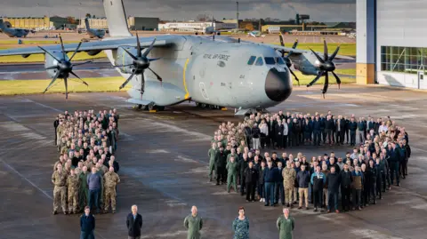 RAF personnel celebrating on the tarmac at RAF Brize Norton by forming a one and zero (10) in front of the plane.