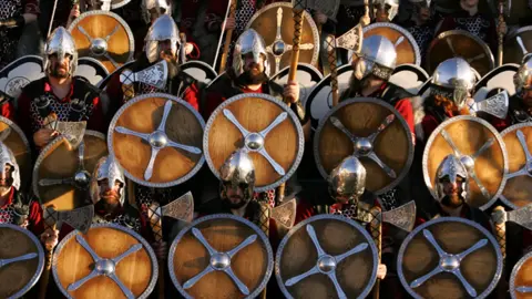 An image showing a reenactment in Shetland Islands, Scotland, depicting Vikings with helmets and circular shields.