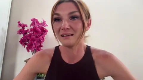 Jade Belgrove speaks to the BBC on a video call with a pink flower behind her