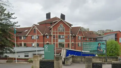 Google Entrance to Spire Healthcare hospital, with green sign outside saying "Spire" and an image of a heart in white.