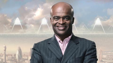 Kriss Akabusi stood in a suit in front of a backdrop of London