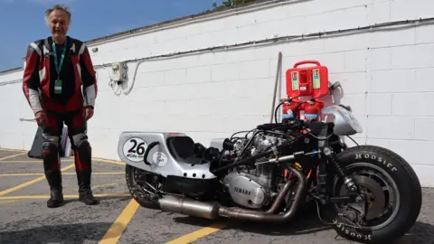 Rob standing next to his old sidecar racer, which is parked near a white wall. 