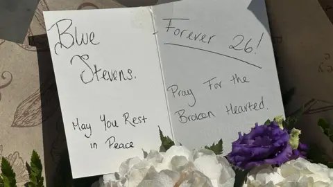 A card tribute to Blue Stevens who died on Wednesday saying "Blue Stevens, may you rest in peace, pray for the broken-hearted. Forever 26."