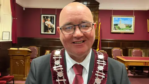 William Walker dressed in a suit and wearing a chain and floret stands in a lodge room