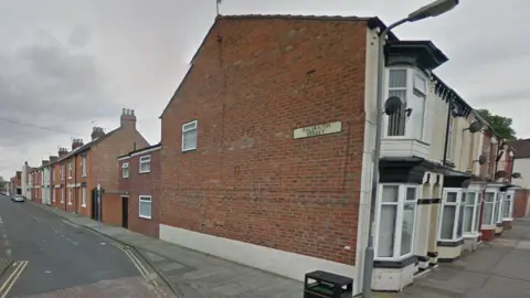 Falmouth Street in Middlesbrough. The street sign is attached to the side of a terraced house on an adjacent building. A row of red-brick terrace houses line Falmouth Street. There are parking bays in the road but few cars.