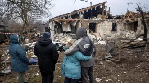 Reuters Four people in winter jackets look at ruined house. 
