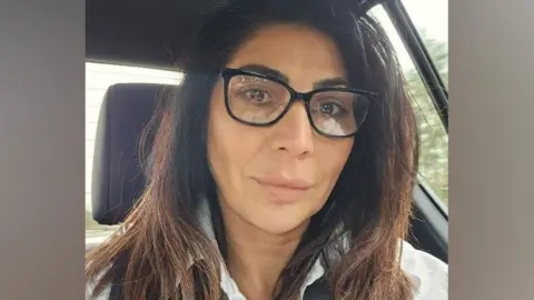 Sandy Joseph looking straight at the camera, with dark hair,dark framed glasses and a white collared shirt.