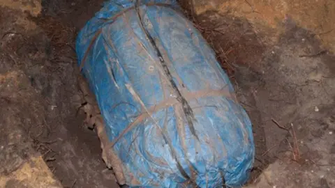 Kent Police A hole in the ground with a large blue package wrapped in blue plastic and tied up with tape.