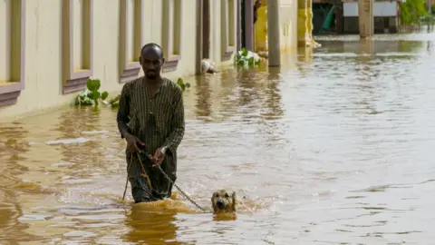 Getty Images A Sudanese man wades through the floodwaters with his dog at Umm Dawm district in Khartoum, Sudan on September 8, 2020.