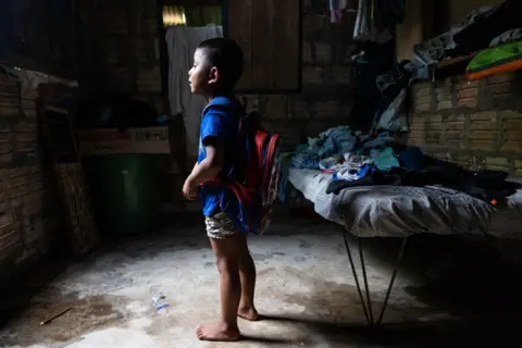 Fernanda Pineda A child stands in a hut with his school backpack