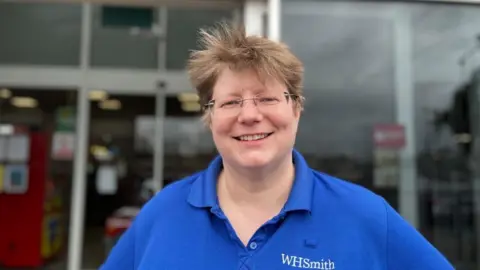 Ollie Conopo/BBC Jen Roberts with short fair hair and glasses wearing a WH Smith t-shirt