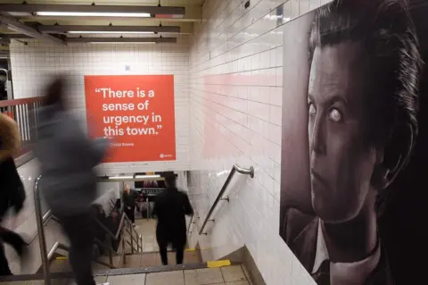 Angela Weiss / AFP People walk by an David Bowie art installation