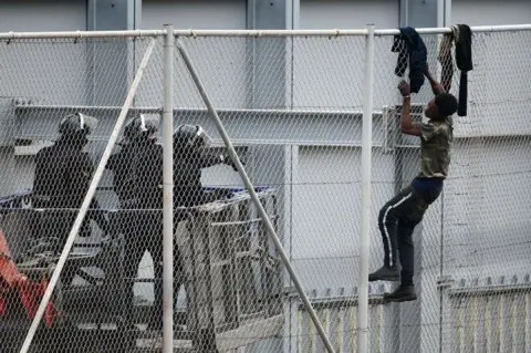 AFP A man attempts to scale a fence as border guards stand on the other side.