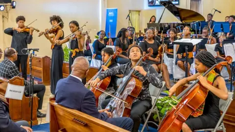 Gemma Hazelwood Members of the Kanneh-Mason family (Sheku plays the cello front centre) during a performance with the Antigua and Barbuda Youth Symphony Orchestra