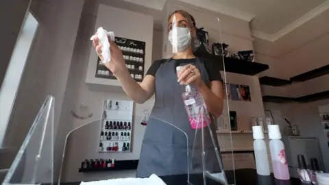 Martin Rickett/PA Media Roberta Dyer, owner of Roberta Beauty Redefined in Knutsford, Cheshire, wears PPE while she cleans a protective screen as they prepare to reopen