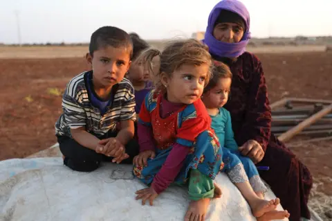 AFP Syrian children and a woman sit near a camp for displaced civilians in Idlib province, Syria (1 September 2018)