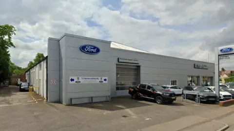 Google The TC Harrison Ford garage in St Neots - a grey coloured showroom and repair centre with vehicles parked on the forecourt