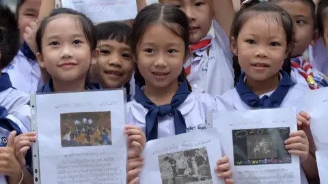 AFP Thai students smile as they hold pictures of 12 boys and a football coach at a school in front of hospital where the boys rescued