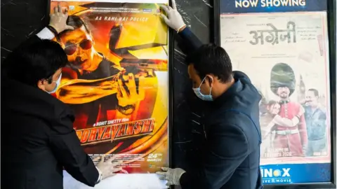 Getty Images Workers put up movie posters in a theatre ahead of the scheduled reopening of cinema theatres on October 15