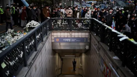 Reuters A police officer stands guard at the exit of a subway station as people gather to pay their respects following a crowd crush that happened during Halloween festivities, in Seoul, South Korea, November 1, 2022.