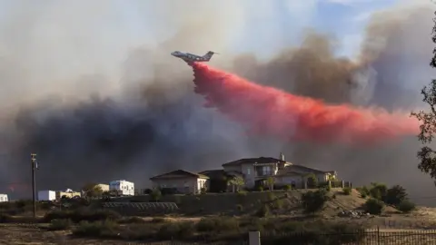 Getty Images A plane drops fire retardant near a home to stop the wind driven Liberty Fire near Los Alamos Road on 7 December 2017 in Murrieta, California