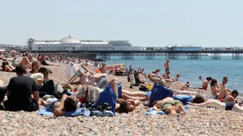 PA People relax in the sunshine on the beach in Brighton, Sussex