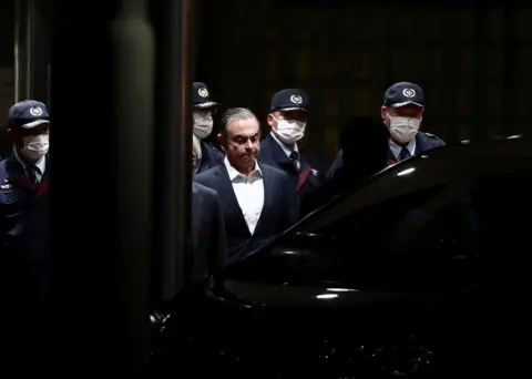 Behrouz Mehri / AFP Former Nissan chairman Carlos Ghosn is escorted out of the Tokyo Detention House in April following his release on bail for multiple charges of financial misconduct.