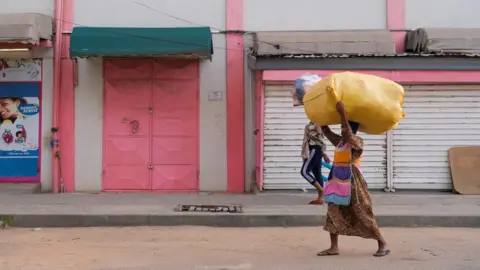 Reuters Two women with loads on their heads walk in front of a closed shops