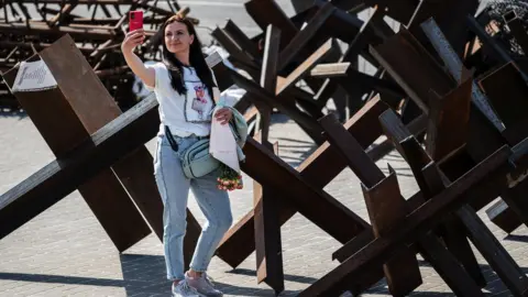 Reuters A woman takes a selfie by anti-tank barricades in Kyiv