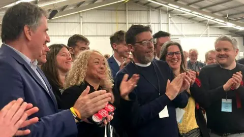 Candidate Peter Norris (centre in black) wins by one vote. Steve Rotheram and Liverpool riverside MP Kim Johnson join in celebration