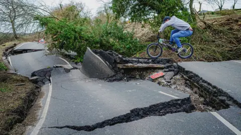 PA Media BMX rider jumping off a ledge on a road badly damaged by subsidence