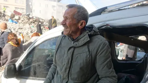 A man stands by a crumpled car