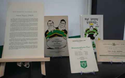Northampton Saints Foundation Several old documents and books that are Northampton Saints related on a table.