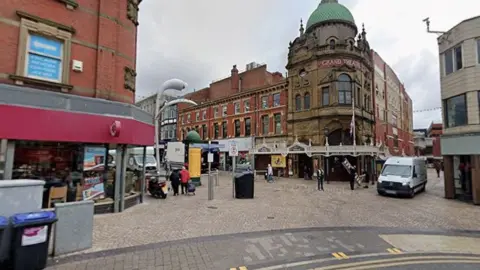 A street view of Blackpool town centre with the Grand Theatre in the centre and rows of shops going off to each side of the street. 