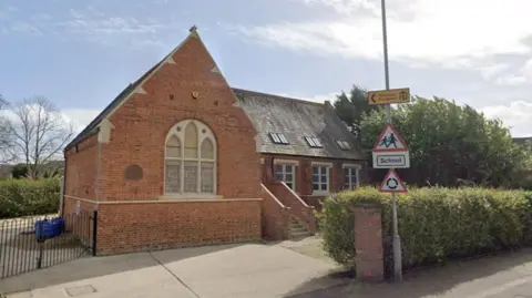 A single-storey brick-built building. Facing the road is a pitched roof, with a very large arched window. The rest of the building is at right angles to it and steps can be seen going up to its door. 