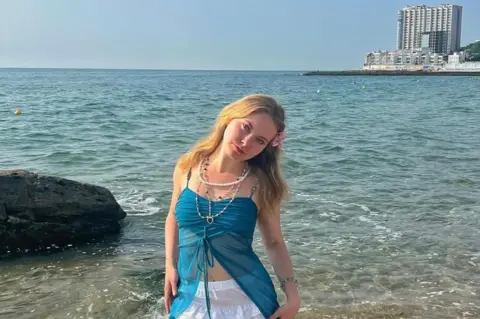 Alena Somova Anastasiia is standing in the middle of the shot on the shore of Odesa Black Sea. With the sea behind her.
