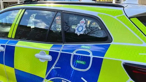 A side view of a marked police car featuring yellow and blue reflective panels. The Humberside Police crest is visible on a rear window.
