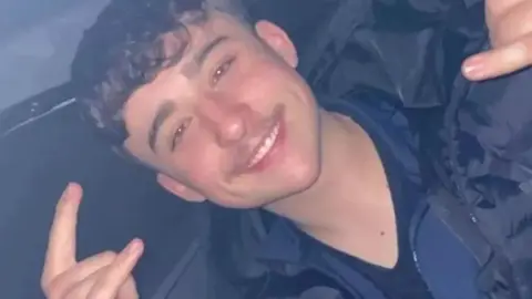 BBC Owen Dunn smiling into a camera, holding his fingers in the air