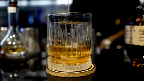 Whisky in tumbler on bar with drinks bottles.