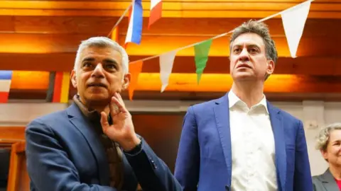 PA Media Sadiq Khan and Ed Miliband listening to someone as they visit a school in north London