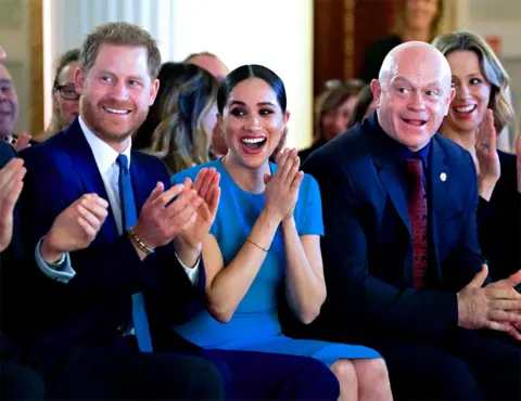 Paul Edwards / Getty Images Harry, Meghan and Ross Kemp cheer to a wedding proposal