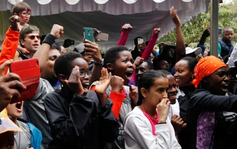 Njeri Mwangi/Reuters People celebrate as they watch Eliud Kipchoge run a marathon