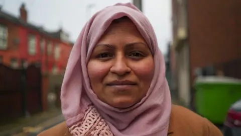 BBC Shuheda, a woman wearing a pink hijab and brown coat, stood on a street outside the food hub