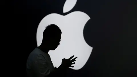 Reuters of a man holding a smartphone in front of a lit-up Apple logo.