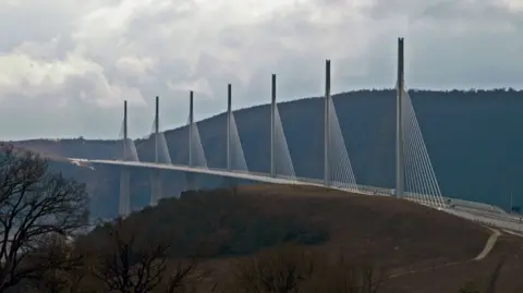The Millau Viaduct spanning a large valley. It is white and parts of it looks like sails.