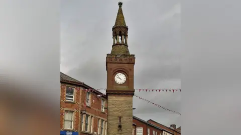 View of the top of the historic Ormskirk Clock Tower on a grey cloudy day.