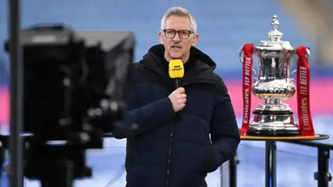 Getty Images Gary Lineker, BBC Sport TV Pundit speaks whilst standing next to the FA Cup trophy prior to the Emirates FA Cup Quarter Final match between Leicester City and Manchester United at The King Power Stadium on March 21, 2021