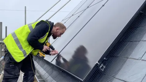 Ben Schofield/BBC An installer working on an array of solar panels